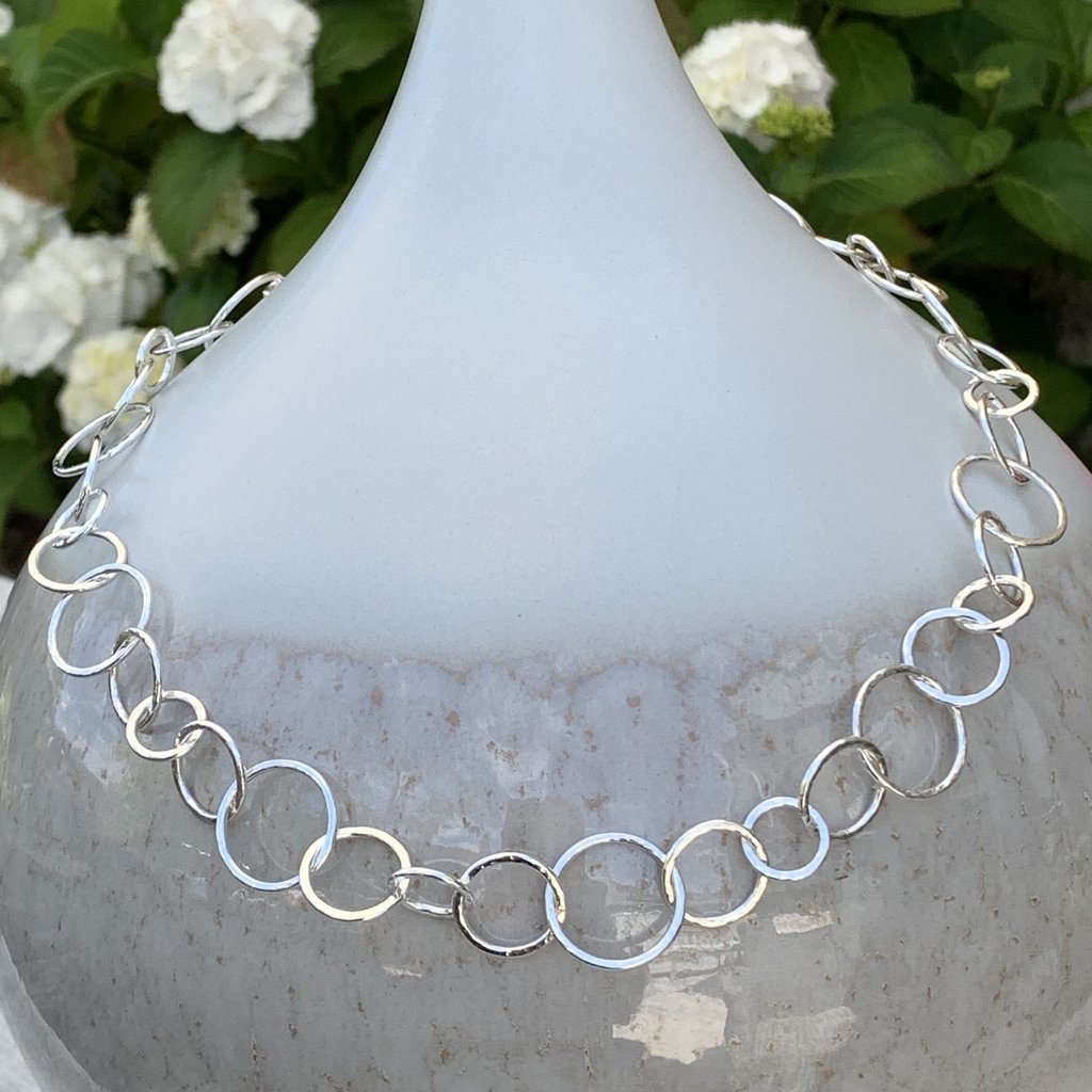 Caldera Cirque Link - 20" handmade hammered silver necklace - displayed on vase